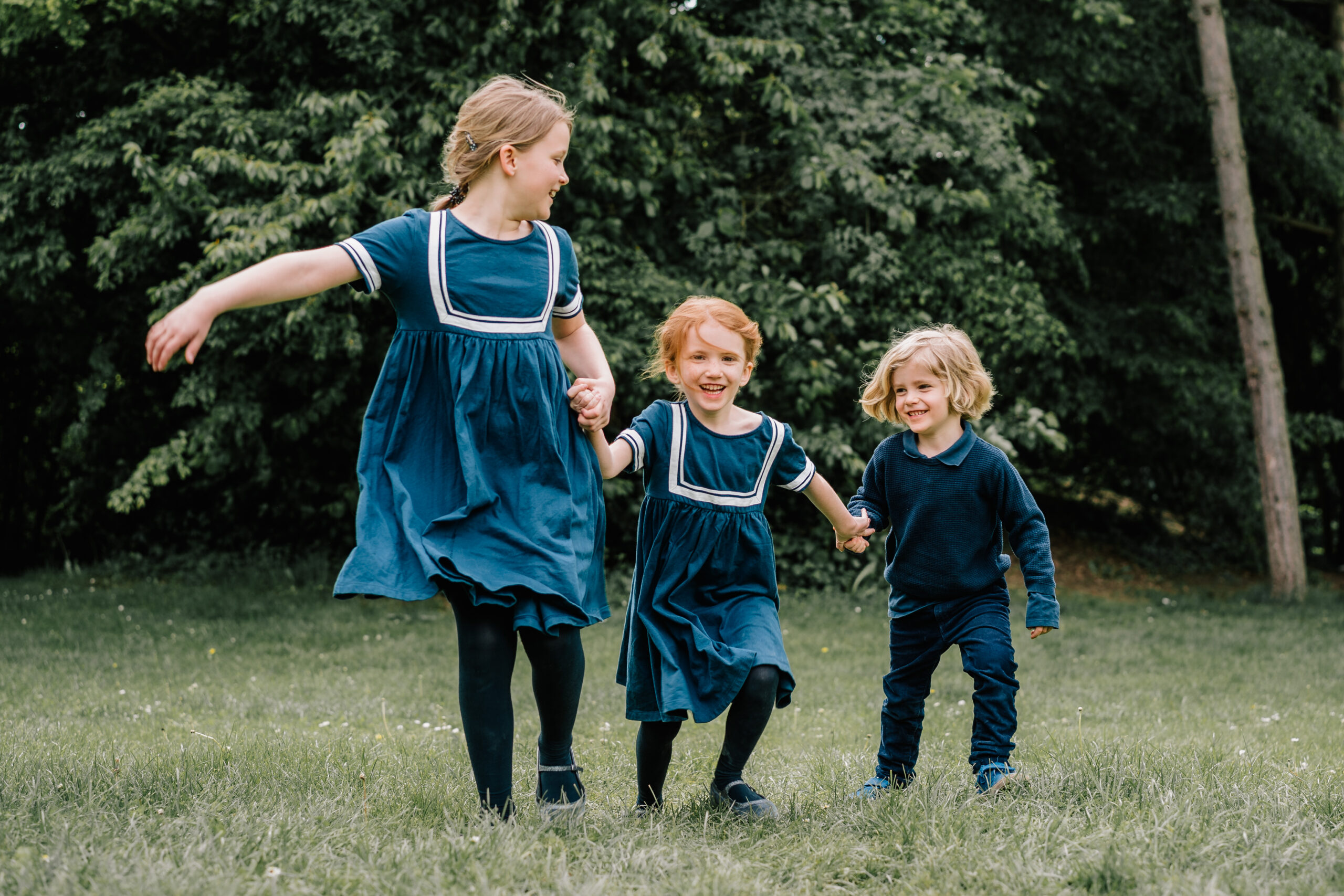 Kindergartenfotos von drei Geschwistern, die sich an der Hand halten und zusammen über die Wiese laufen.