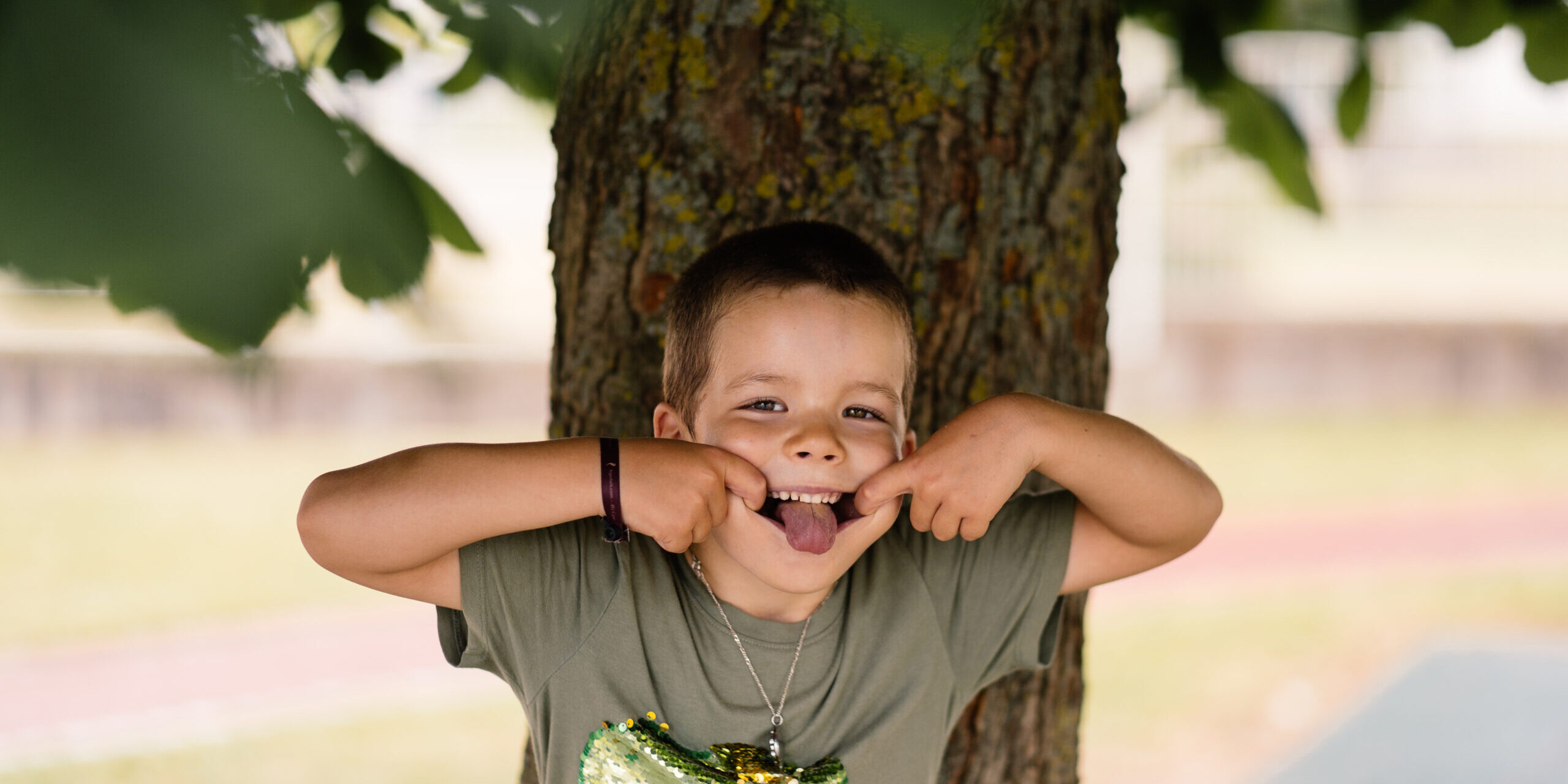 Kindergartenfoto von einem Jungen unter einem Baum, der eine Grimasse schneidet.